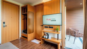 Ein modernes Zimmer mit einem Holzschrank, einem Flachbildfernseher, der "PLAYOTEL RESORT" zeigt, einem kleinen Tisch mit Wasserkocher, Tassen und einer Pflanze.