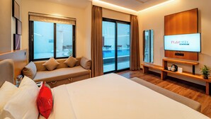 Ein modernes Hotelzimmer mit einem großen Bett, einer Sitzecke, einem Fernseher und einem Balkon mit Blick.