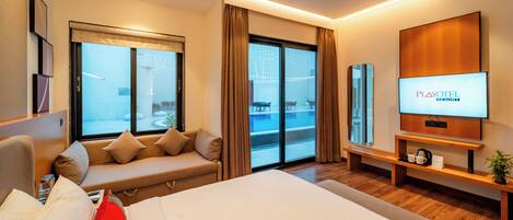 A modern hotel room with a large bed, a sofa, a TV, and a balcony with a view.
