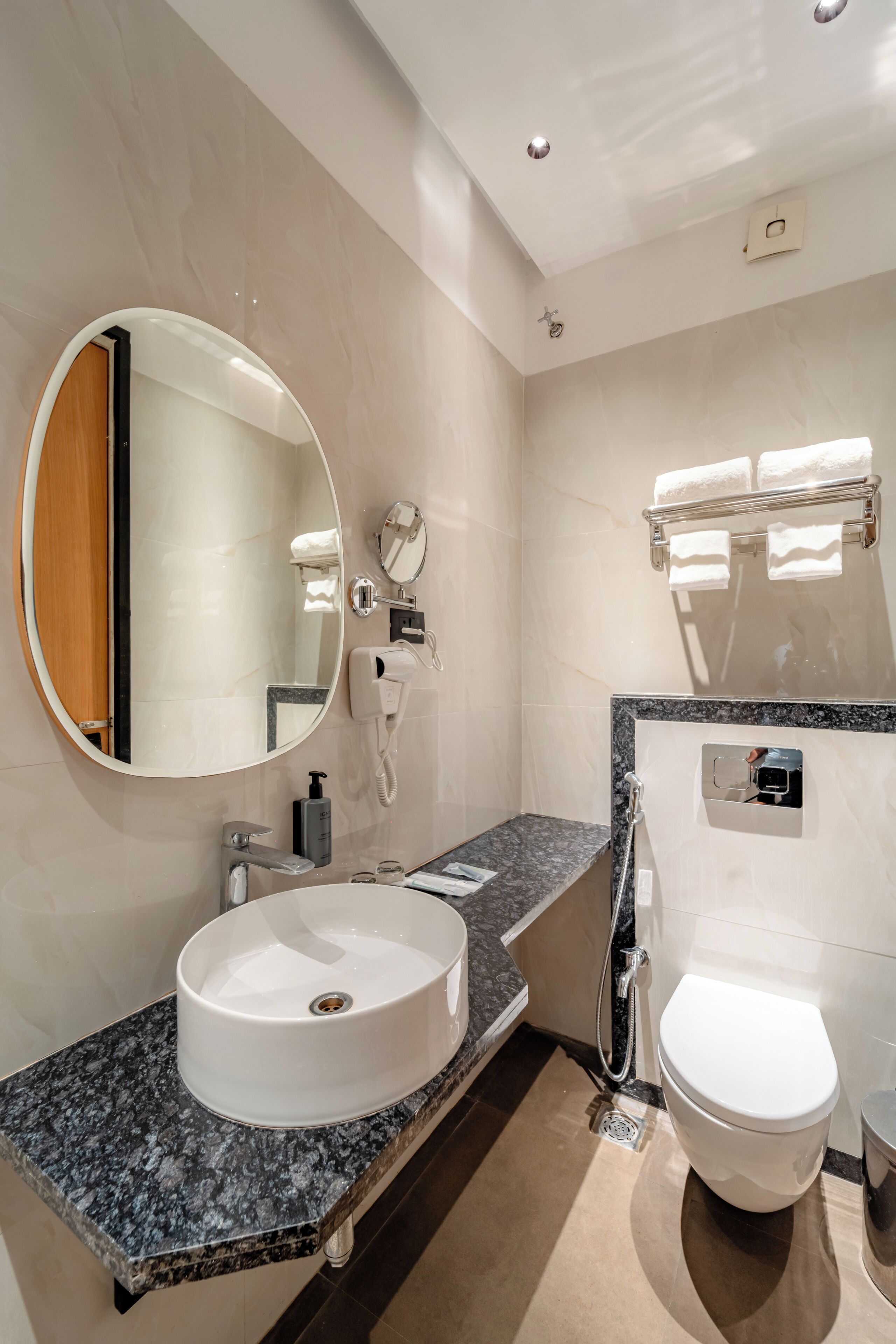 Et moderne badeværelse med et rundt håndvask, toilet, spejl og håndklædestang.
