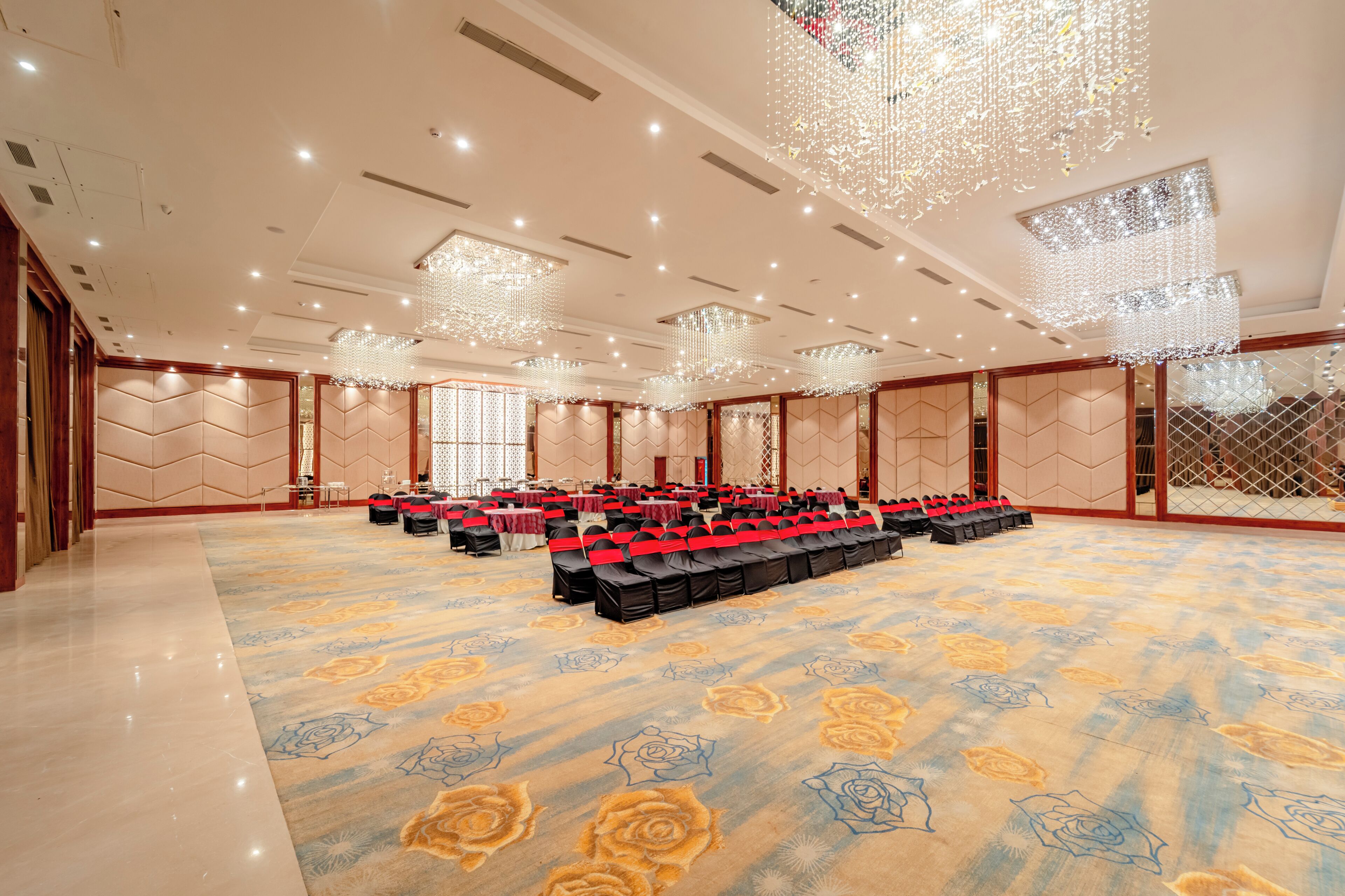 Un amplio salón de banquetes con filas de mesas y sillas, grandes candelabros y una alfombra estampada.