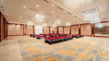 Un amplio salón de banquetes con filas de mesas y sillas, grandes candelabros y una alfombra estampada.