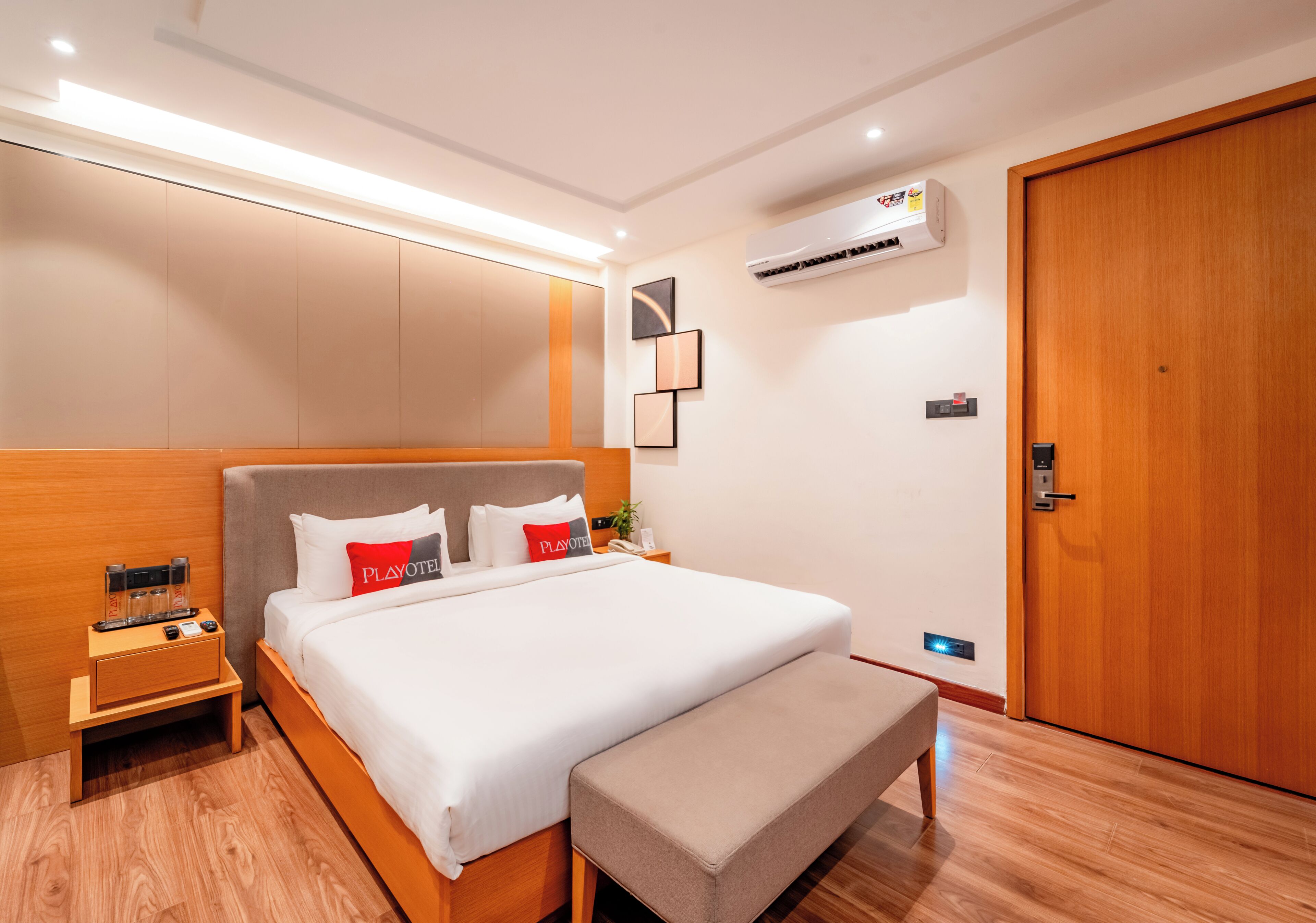 Ein modernes Hotelzimmer mit einem großen Bett, Nachttischen, einer Bank, einer Klimaanlage und einer Holztür.