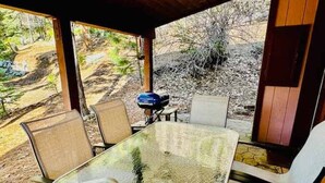 Un espace extérieur abrité, aménagé pour les repas, avec une table et des chaises en verre, le tout entouré d’un paysage naturel.