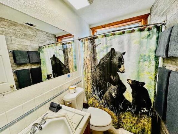 Un baño con cortina de ducha temática de oso, un lavamanos y un inodoro.