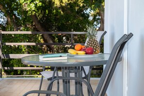 Een ronde glazen tafel met een metalen stoel, een boek en een schaal fruit, waaronder ananas, bananen en appels.