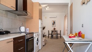 A compact kitchen with a washing machine, a dining area with a table and chairs, and a breakfast setup with orange juice and pastries.