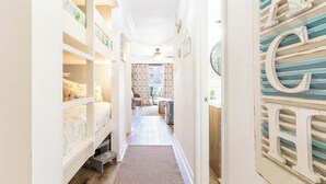 Un couloir étroit, orné d’un tapis à motifs, avec un lit superposé sur la gauche et un mur décoratif sur lequel sont disposées des lettres.