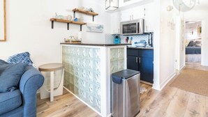 Une cuisine compacte avec un îlot central, un four à micro-ondes et un évier. Le salon comprend un canapé bleu et une petite table ronde.