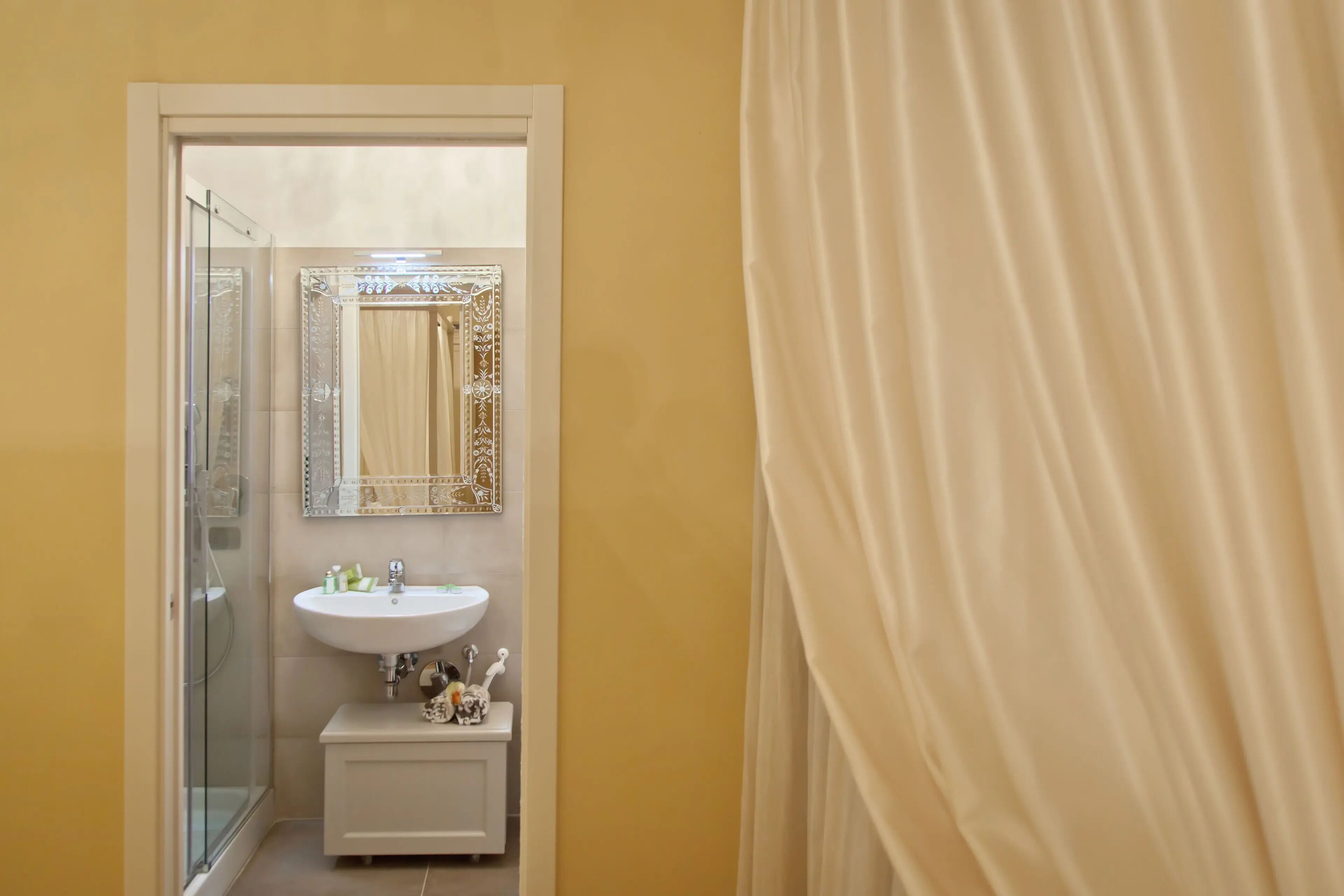 A bathroom with a glass shower enclosure, a white sink, and a mirror with a decorative frame.
