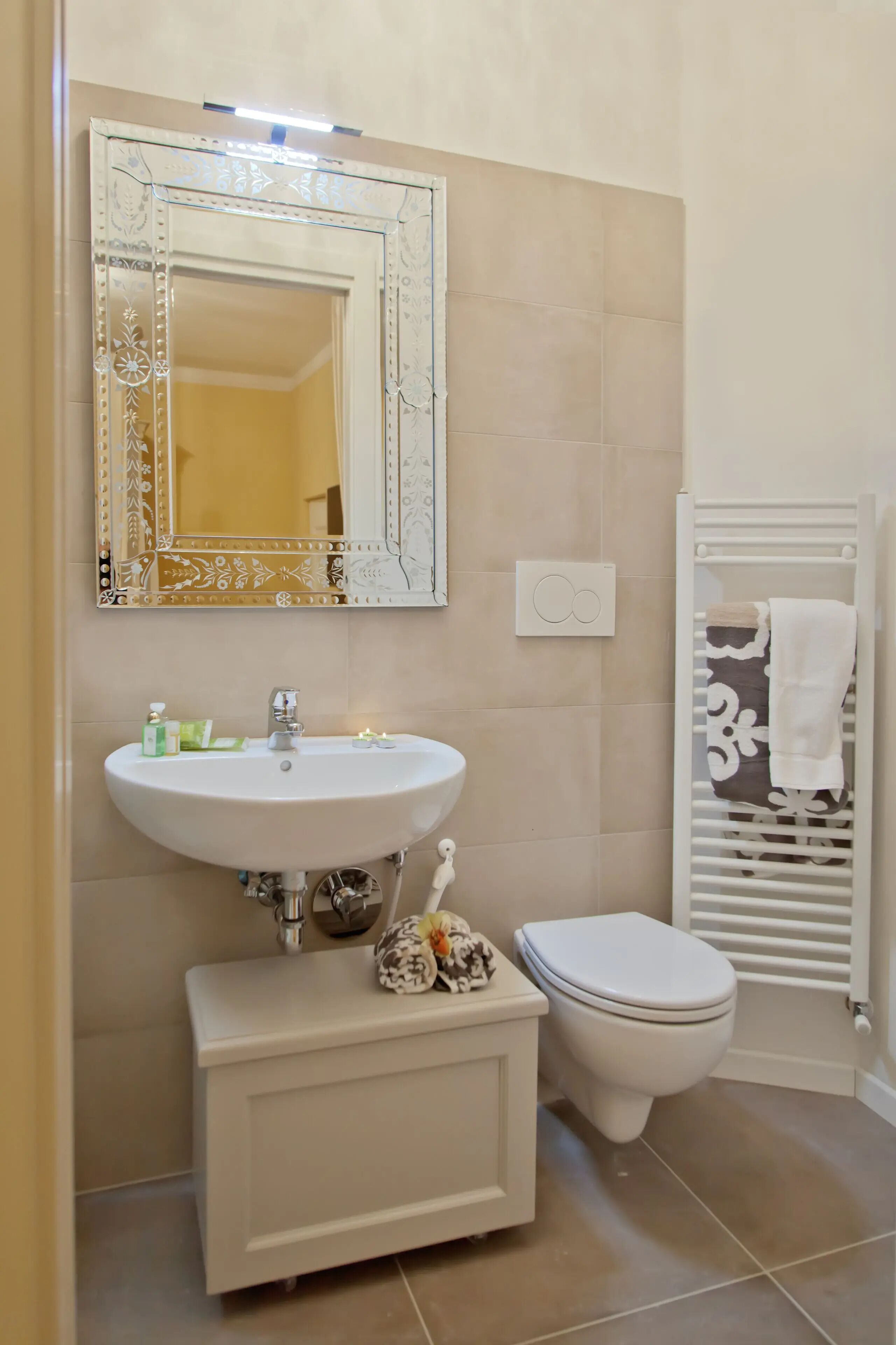 Een badkamer met een wit wastafelmeubel, een spiegel met decoratieve lijst, een toilet en een handdoekhouder.