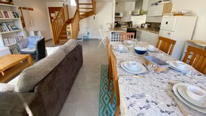 A modern kitchen with white cabinets, a microwave, and a refrigerator. There is a dining area with a table set for four, chairs, and a staircase leading to an upper level. - MASSALINE - Holiday home between town and beaches, Carnac - K38 (Carnac)