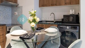A modern kitchen with wooden cabinets, a built-in stove, a microwave, and a washing machine. - Bloomfields Stylish 1BR In Oasis Masdar City (Abu Dabi)