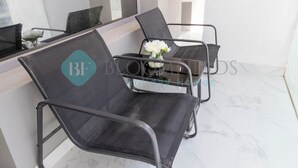 A modern hotel room with a marble floor, a glass table, and two black mesh chairs with a vase of white flowers. - Bloomfields Stylish 1BR In Oasis Masdar City (Abu Dabi)
