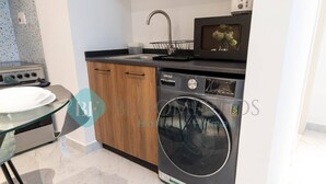 A compact kitchen with a washing machine, a microwave, and a sink. - Bloomfields Stylish 1BR In Oasis Masdar City (Abu Dabi)