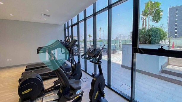 Et fitnesscenter med løbebånd og motionscykler, store vinduer samt udsigt til palmer og bygninger.