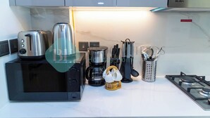 Et moderne køkken med en sort mikrobølgeovn, kaffemaskine, brødrister og gasblus.