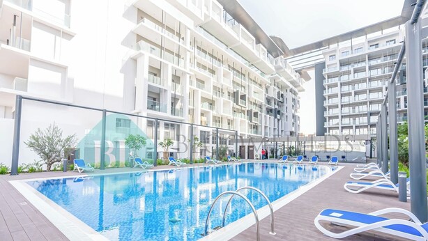 Een zwembad op het dak met blauw water, omringd door ligbedden en een modern gebouw met balkons.