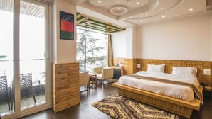 A modern bedroom with a large bed, a wooden headboard, a desk, and a view through a sliding glass door. - THE SIDDHARTHA (Dharamshala)