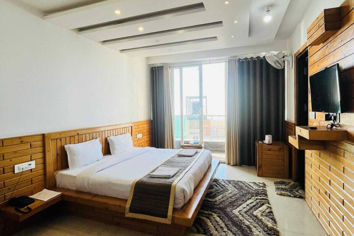 A modern hotel room with a wooden bed, a flat-screen TV, and a large window with curtains.
