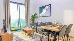 Un salon moderne comprenant un canapé, une table à manger et des chaises, un téléviseur posé sur un meuble en bois, et une grande fenêtre avec des rideaux.
