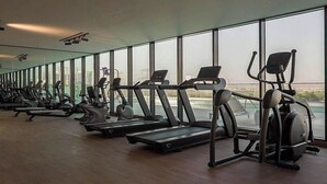 Una palestra con diverse tapis roulant e cyclette, ampie finestre e vista sui palazzi.