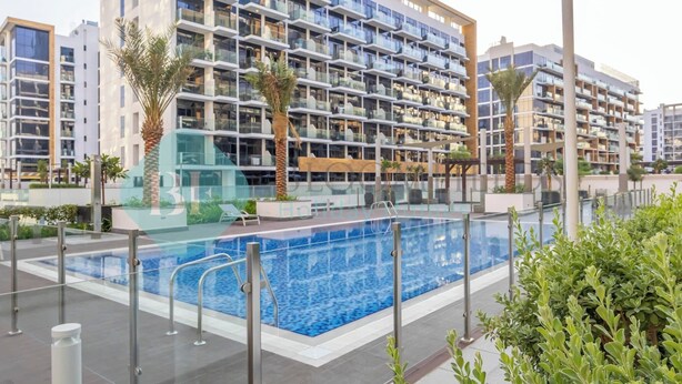 A modern hotel with a large outdoor swimming pool, multiple balconies, and lush landscaping.