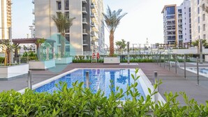 A modern residential building with a swimming pool, surrounded by greenery and palm trees.