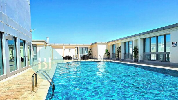 A swimming pool with a tiled deck, surrounded by a building with large windows and a balcony. - Bloomfields Hidden Gem 1BR In ElYacout Tower (Abu Dabi)