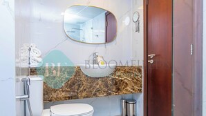 A bathroom with a marble countertop, a toilet, a shower, and a wooden door. - Bloomfields Hidden Gem 1BR In ElYacout Tower (Abu Dabi)