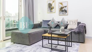 A modern living room with a grey sectional sofa, a wooden coffee table, and two framed botanical prints on the wall. - Bloomfields Hidden Gem 1BR In ElYacout Tower (Abu Dabi)