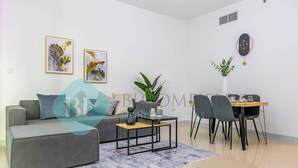 A modern living room with a grey sofa, a coffee table, and a dining area with a table and chairs. - Bloomfields Hidden Gem 1BR In ElYacout Tower (Abu Dabi)