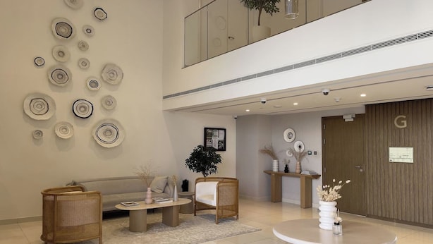 Un hall d’entrée moderne avec un plafond haut, un comptoir de réception, un canapé, deux fauteuils, une table basse et un mur décoratif orné de motifs circulaires.