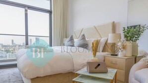Habitación de hotel moderna con una cama grande, un escritorio con una computadora portátil, una mesita de noche con una lámpara y vistas a la ciudad a través de grandes ventanales.