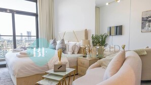Een moderne hotelkamer met een groot bed, een bank, een bureau met een laptop, een televisie en uitzicht over de stad.