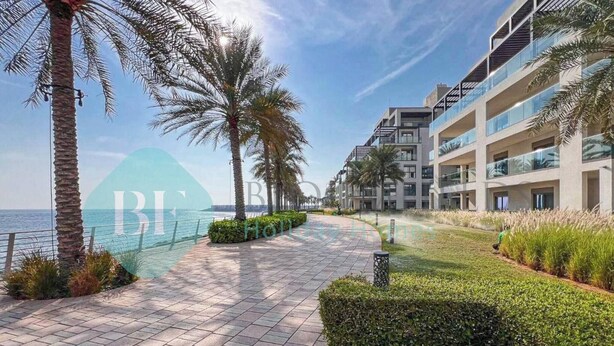 A modern hotel with a paved walkway, palm trees, and a view of the sea.