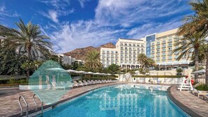 A swimming pool with lounge chairs and umbrellas, surrounded by palm trees and a mountain in the background.