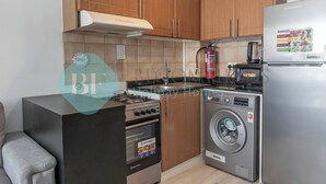 Une cuisine moderne avec des meubles en bois, une cuisinière à gaz, un four encastré, un lave-linge et un réfrigérateur.