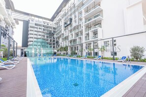 A modern hotel with a swimming pool, sun loungers, and a glass facade.