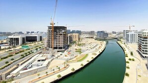 A modern urban area with a river, construction cranes, and high-rise buildings.
