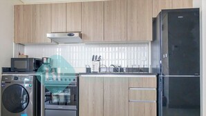 A kitchen with wooden cabinets, a black refrigerator, a microwave, a washing machine, and a coffee maker.