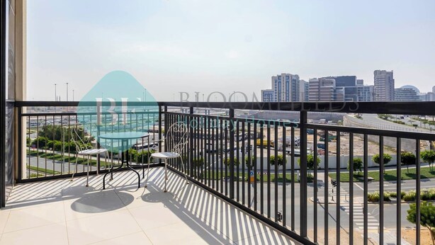 A balcony with a glass table and chairs, overlooking a cityscape with modern buildings and a road.