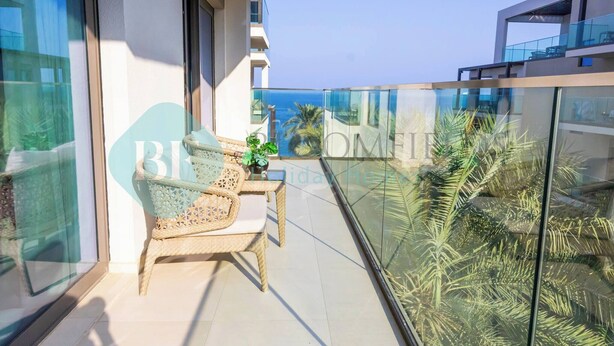 A balcony with wicker furniture, a glass railing, and a view of the sea. - Bloomfields Iconic 2BR & Maid Address Beach Resort (Fujairah)