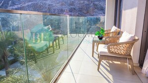 A balcony with wicker furniture, a glass railing, and a view of a rocky landscape. - Bloomfields Iconic 2BR & Maid Address Beach Resort (Fujairah)