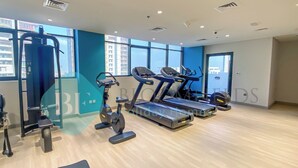 A modern gym with cardio machines, a weight bench, and a wall-mounted exercise machine. - Bloomfields Modern STU In Azizi Riviera (Dubai)