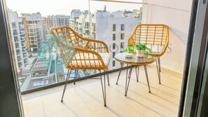 A balcony with wicker chairs and a small table, overlooking a residential area with modern buildings. - Bloomfields Modern STU In Azizi Riviera (Dubai)