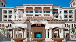 A large, multi-story hotel with a central courtyard, featuring a fountain, palm trees, and a blue door. - Bloomfields 1BR St Regis in Saadiyat (Abu Dhabi)
