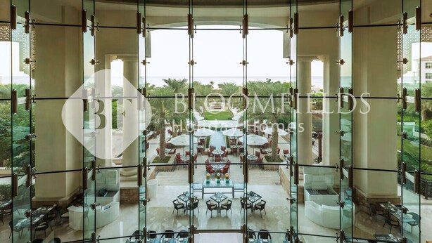 A luxurious indoor dining area with a glass ceiling, offering a view of a landscaped outdoor patio. - Bloomfields 1BR St Regis in Saadiyat (Abu Dhabi)