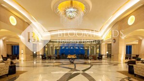 A spacious lobby with a grand chandelier, comfortable seating, and a blue backdrop at the far end. - Bloomfields 1BR St Regis in Saadiyat (Abu Dhabi)