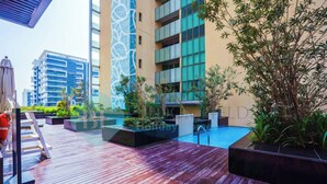 A rooftop pool area with wooden decking, potted plants, and a lifeguard chair. - Bloomfields Adorable 1BR in Raha Beach Access (Abu Dabi)